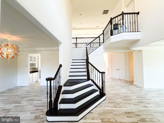 staircase featuring crown molding, wood finished floors, visible vents, and wainscoting