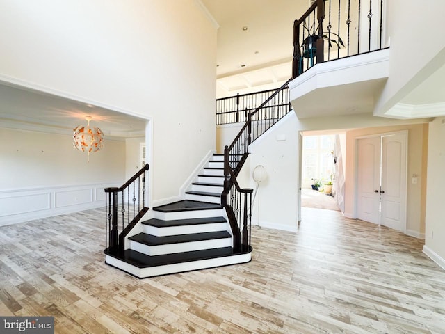 stairway featuring a decorative wall, ornamental molding, a towering ceiling, and wood finished floors