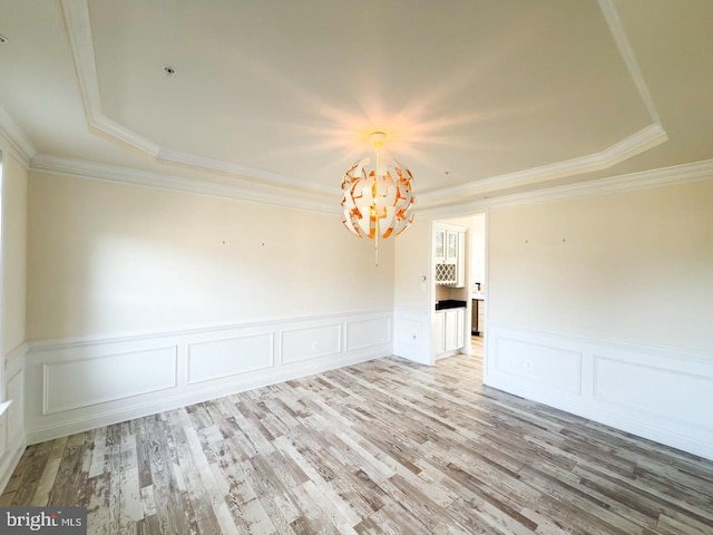 spare room featuring light wood finished floors, a chandelier, crown molding, and a raised ceiling