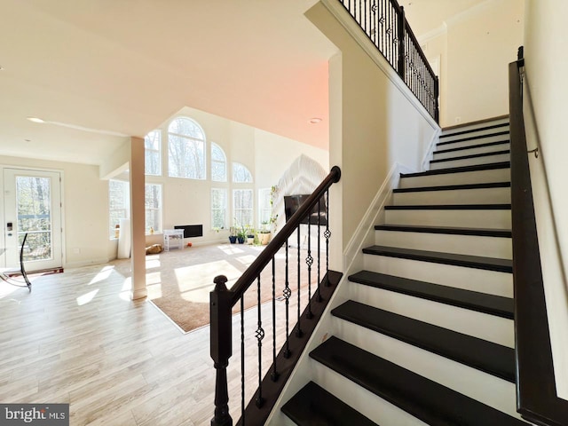 stairway with baseboards, wood finished floors, and a towering ceiling