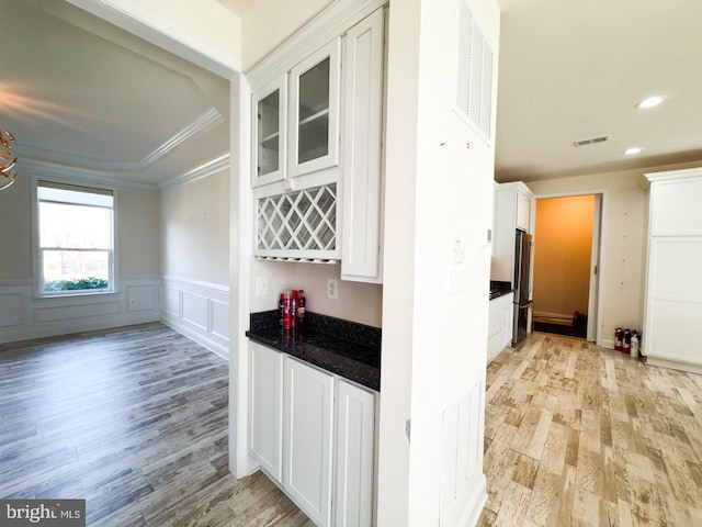 kitchen featuring light wood-type flooring, white cabinetry, freestanding refrigerator, wainscoting, and crown molding