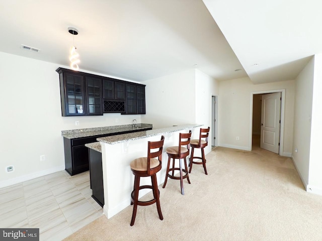 kitchen with visible vents, glass insert cabinets, baseboards, light stone countertops, and a kitchen breakfast bar