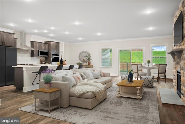 living room featuring a stone fireplace, recessed lighting, crown molding, and wood finished floors