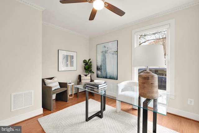 sitting room with wood finished floors, a ceiling fan, visible vents, baseboards, and crown molding