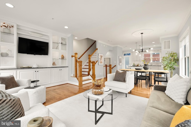 living area with light wood-style floors, visible vents, stairway, and crown molding