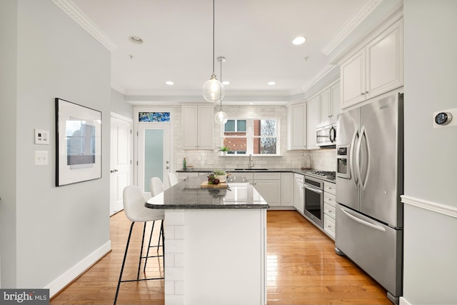 kitchen featuring crown molding, backsplash, appliances with stainless steel finishes, white cabinetry, and a kitchen island