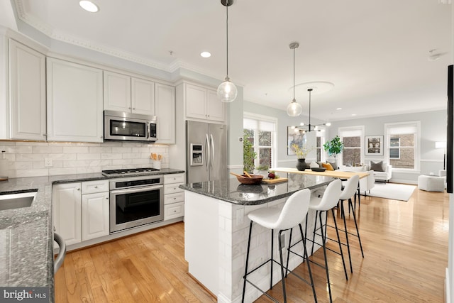 kitchen featuring tasteful backsplash, dark stone countertops, stainless steel appliances, light wood-style floors, and white cabinetry