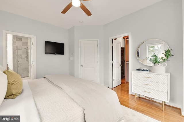 bedroom featuring light wood finished floors, a ceiling fan, connected bathroom, a walk in closet, and a closet