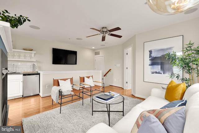 living area featuring light wood-style flooring, visible vents, a ceiling fan, baseboards, and indoor wet bar