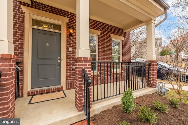 view of exterior entry featuring covered porch and brick siding