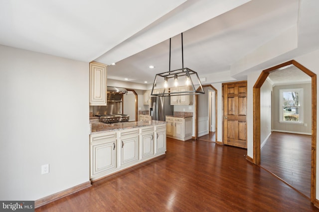 kitchen with light stone counters, arched walkways, cream cabinetry, dark wood finished floors, and stainless steel fridge