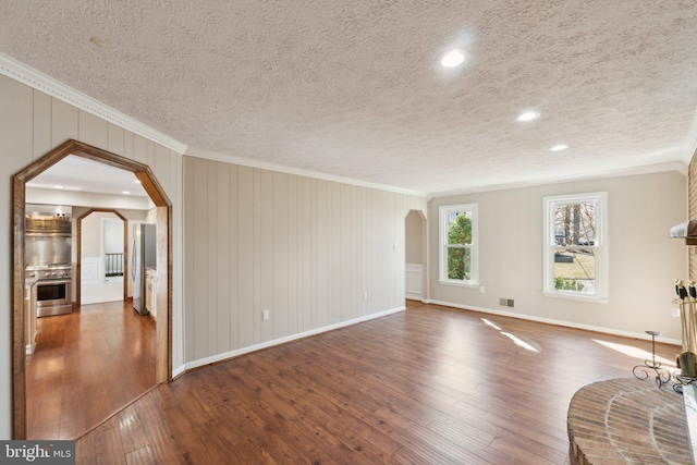 unfurnished living room with arched walkways, baseboards, hardwood / wood-style flooring, and crown molding