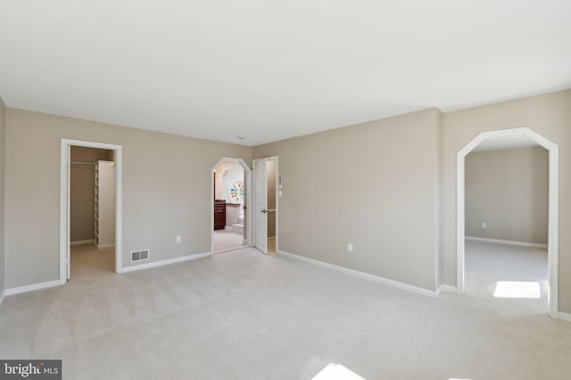 interior space with light carpet, visible vents, arched walkways, and baseboards