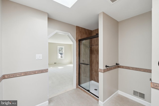 bathroom with tiled shower, a skylight, visible vents, and baseboards