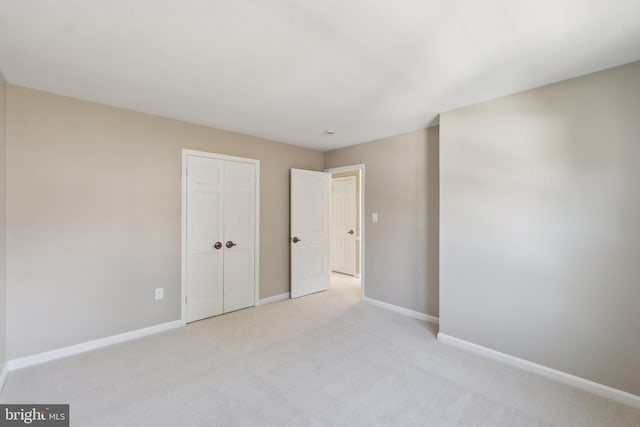 unfurnished bedroom featuring light carpet, a closet, and baseboards