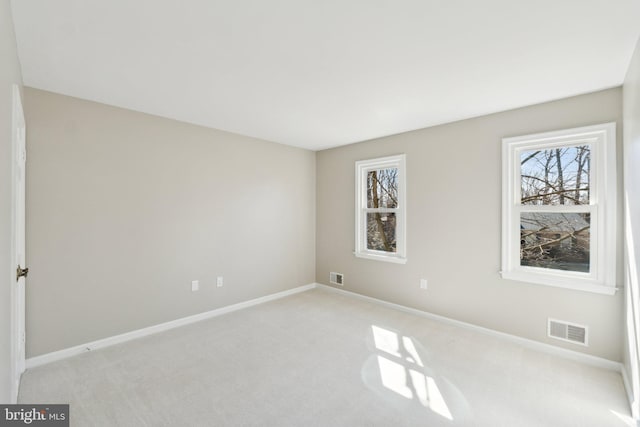 spare room with visible vents, plenty of natural light, light carpet, and baseboards