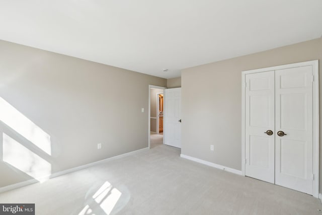 unfurnished bedroom featuring baseboards, a closet, and light colored carpet