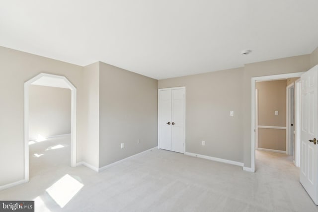 unfurnished bedroom featuring baseboards, a closet, and light colored carpet