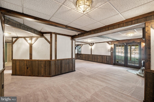 basement with a wainscoted wall, wood walls, a drop ceiling, and carpet