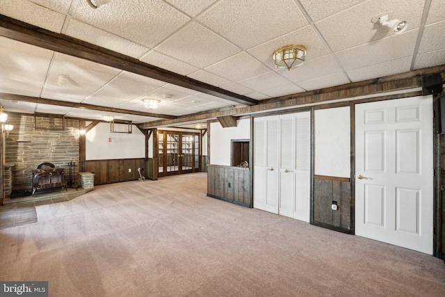 below grade area featuring carpet floors, a wood stove, wainscoting, and a drop ceiling