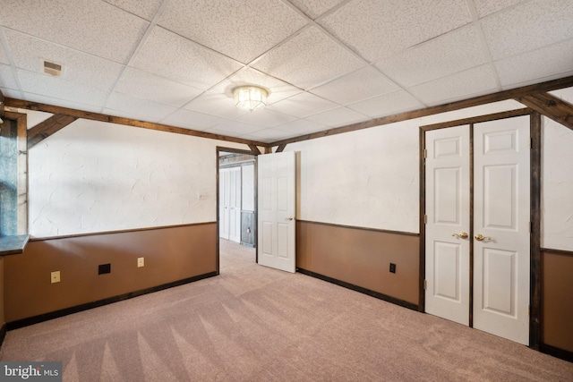 interior space featuring a wainscoted wall, carpet flooring, and a drop ceiling