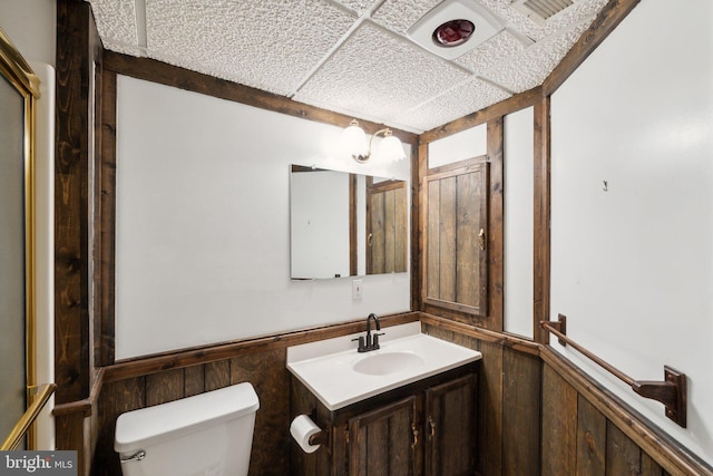 bathroom with a paneled ceiling, a wainscoted wall, vanity, and toilet