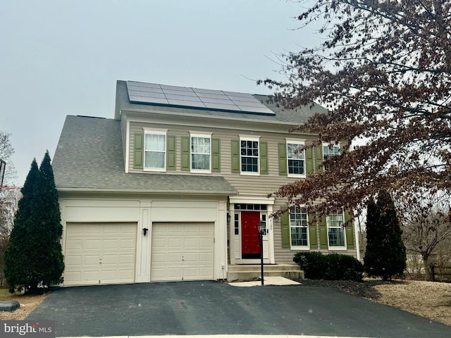 view of front of property featuring driveway, roof with shingles, and roof mounted solar panels