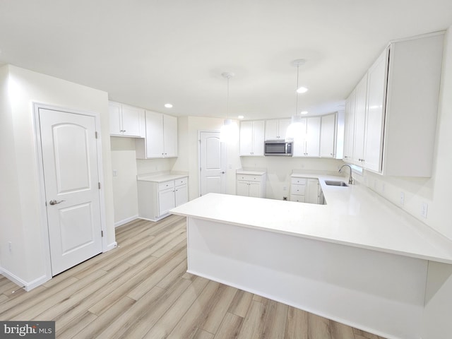 kitchen with kitchen peninsula, hanging light fixtures, light hardwood / wood-style floors, sink, and white cabinets