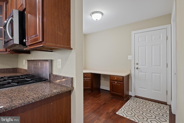 kitchen with baseboards, built in study area, dark wood-type flooring, dark stone countertops, and stainless steel appliances
