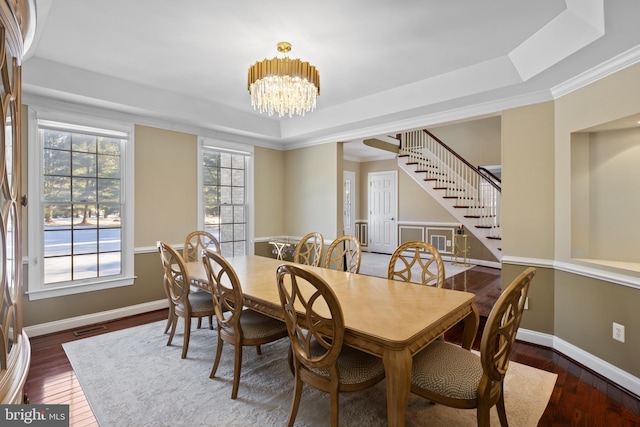 dining area featuring dark wood-type flooring, a tray ceiling, and a notable chandelier