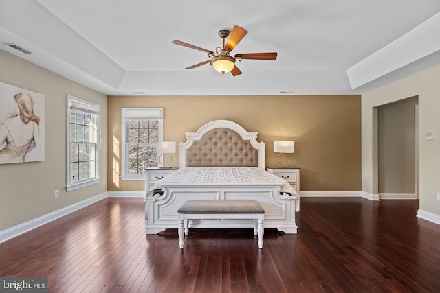 bedroom with a tray ceiling, dark wood finished floors, visible vents, and baseboards