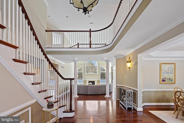 entryway with dark wood-style floors, a fireplace, decorative columns, ornamental molding, and baseboards