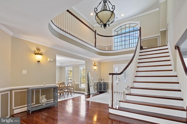 foyer featuring ornamental molding, dark wood-type flooring, a high ceiling, stairs, and a notable chandelier