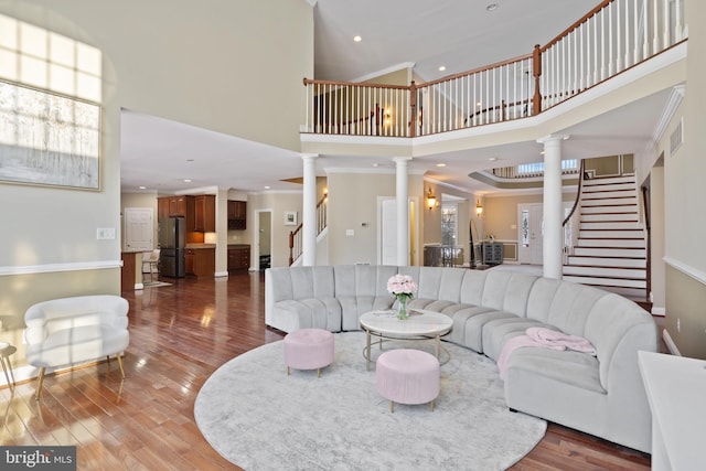 living room featuring a towering ceiling, stairway, ornate columns, and wood finished floors