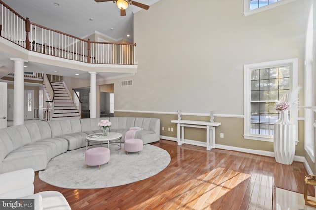 living room featuring visible vents, baseboards, wood finished floors, ornate columns, and high vaulted ceiling