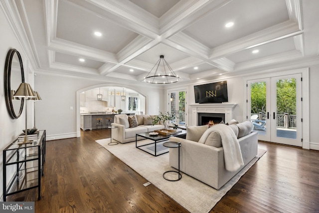 living room with beam ceiling, french doors, dark wood finished floors, a warm lit fireplace, and coffered ceiling