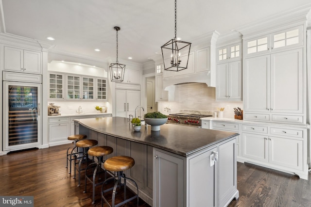 kitchen with wine cooler, premium appliances, a kitchen island with sink, white cabinets, and tasteful backsplash