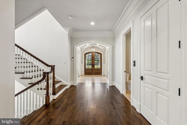 foyer entrance featuring arched walkways, wood finished floors, stairs, crown molding, and french doors