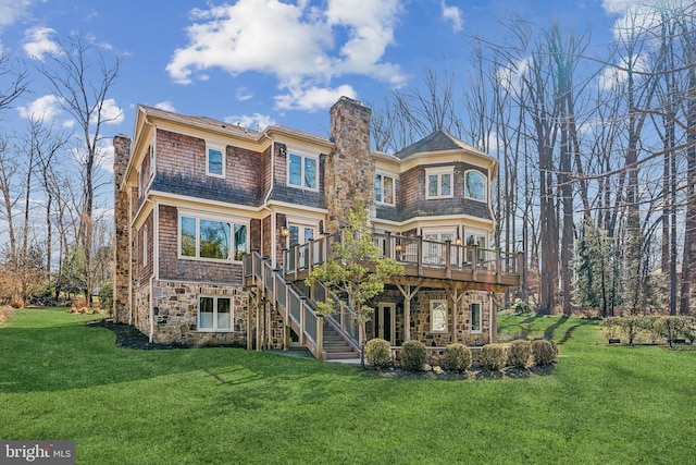 back of property with a deck, stone siding, stairway, a lawn, and a chimney