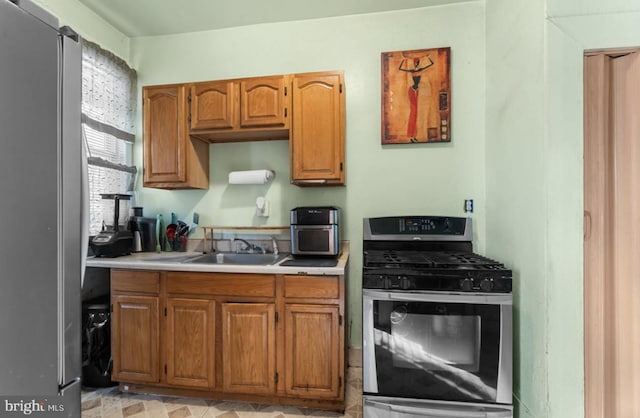 kitchen featuring stainless steel appliances, brown cabinets, light countertops, and a sink