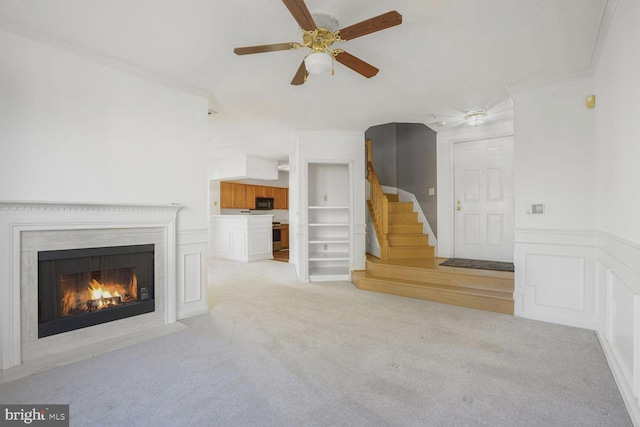 unfurnished living room with ceiling fan, ornamental molding, built in shelves, and light colored carpet