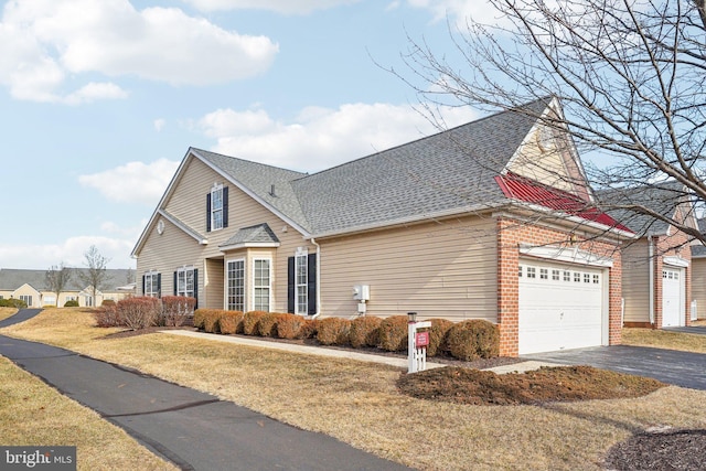 traditional-style house featuring brick siding, roof with shingles, aphalt driveway, and a front yard