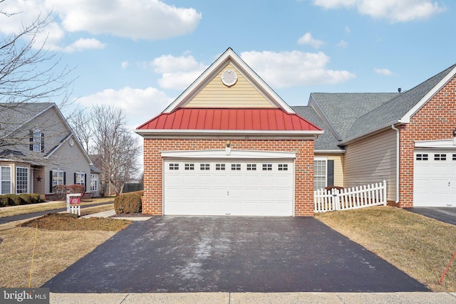 view of front of property featuring driveway, a garage, a standing seam roof, fence, and brick siding