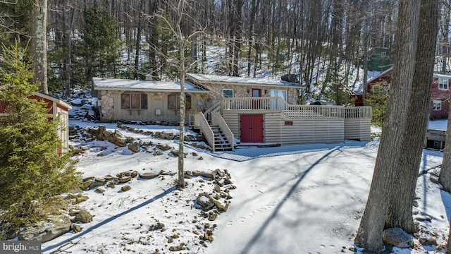 view of front facade featuring stone siding, a wooden deck, and stairs