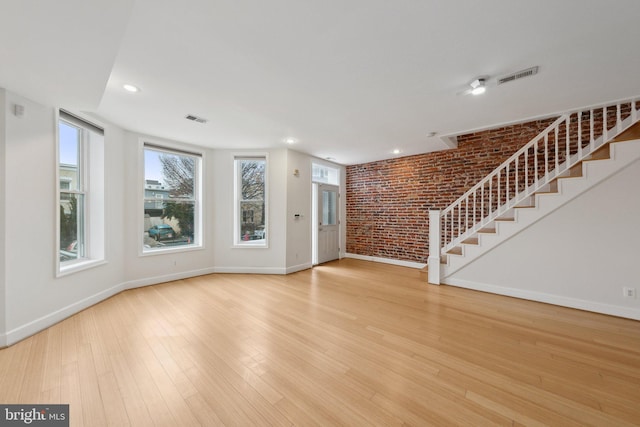 unfurnished living room featuring stairway, brick wall, visible vents, and wood finished floors