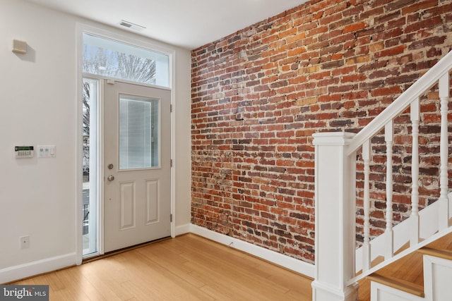 entrance foyer featuring brick wall, baseboards, and light wood-style flooring