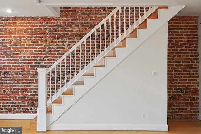 stairs featuring brick wall, wood finished floors, and baseboards