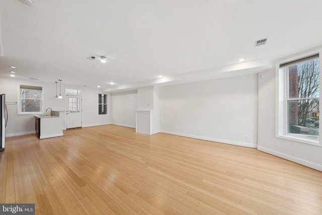 unfurnished living room featuring light wood finished floors, recessed lighting, visible vents, a sink, and baseboards