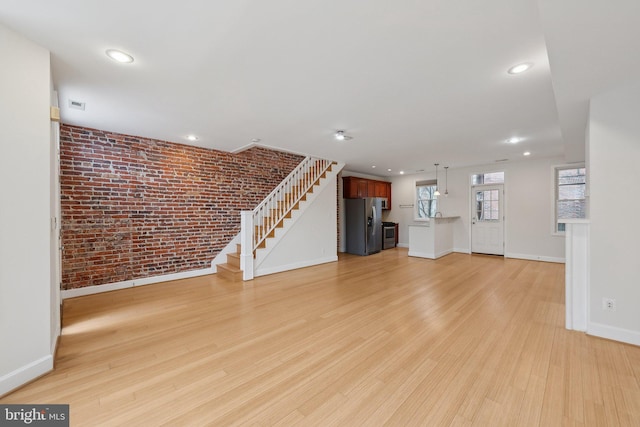 unfurnished living room featuring light wood finished floors, baseboards, brick wall, stairway, and recessed lighting