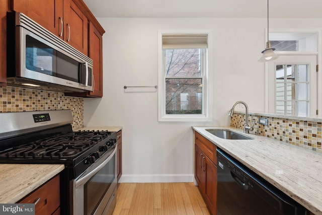 kitchen featuring stainless steel appliances, light wood-style floors, a sink, light stone countertops, and baseboards